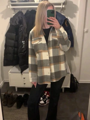 Rutig overshirt från Ivyrevel - Trendig overshirt från Ivyrevel i rutigt mönster med grå, beige och bruna toner. Skjortjackan har knappar framtill, två bröstfickor med lock och klassisk krage. Perfekt att styla lager på lager under höst och vår.