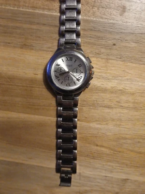 Silverfärgad klocka från Regal - Stilren klocka från Regal i silverfärgat rostfritt stål med länkarmband. Urtavlan är också silverfärgad med romerska siffror och tre mindre dekorativa urtavlor. Klassisk design som passar till många olika stilar.