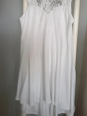 Vit klänning med spetsdetaljer - Säljer en vit ärmlös klänning med vacker spets upptill och knytning i nacken. Klänningen har en luftig och flowy passform, perfekt för varma dagar eller för en skolavslutning.