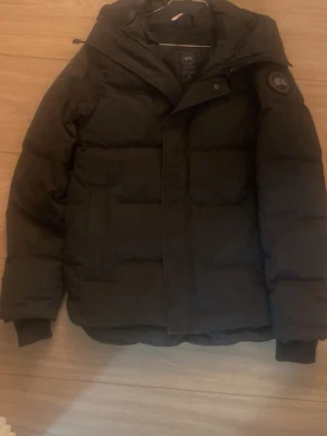 Svart dunjacka från Canada Goose - Säljer en svart dunjacka från Canada Goose med avtagbar pälsdetalj till huvan. Jackan har lång ärm, dragkedja och klassisk patch på ärmen. Perfekt för kalla vinterdagar och riktigt varm. Stilsäker och tidlös modell.