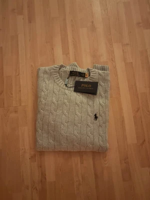 Ralph lauren kabelstickad (M) Ny-oanvänd  - Säljer en helt ny och oanvänd Ralph Lauren kabelstickad tröja i storlek M. Klassisk kabelstickad design i tidlös grå färg med diskret broderad Ralph Lauren-logga på bröstet. Tröjan är tillverkad i hög kvalitet med mjukt och bekvämt material – perfekt för både vardag och mer uppklädda tillfällen. 🔹 Märke: Ralph Lauren 🔹 Modell: Kabelstickad tröja 🔹 Färg: Grå 🔹 Storlek: M 🔹 Skick: Helt ny / oanvänd 🔹 Passform: Klassisk Nypris är högt – perfekt chans att fynda. Hör gärna av dig vid