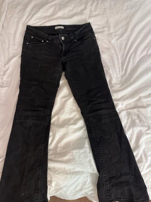 Svarta bootcut jeans - Snygga svarta bootcut jeans med klassisk femficksdesign och knappgylf. Jeansen har en något utsvängd passform nertill och är tillverkade i ett mjukt denimtyg. Perfekta för dig som gillar en tidlös och cool stil. Dem är även lågmidjade 