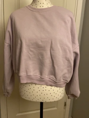 Ljuslila croppad sweatshirt - En stilren ljuslila sweatshirt med croppad passform och rund hals. Tröjan har långa ärmar och ribbade muddar vid ärmslut och nederkant. Perfekt för en avslappnad och trendig look. Materialet känns mjukt och bekvämt mot huden. Lite märklig i storleken. 