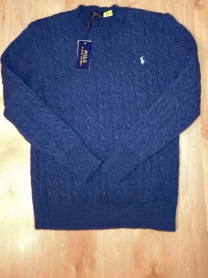 Mörkblå kabelstickad tröja - Riktigt fin Ralph lauren stickad tröja med vit polo Ralph lauren märke vid bröstet. Den är gjord av 100% bomull, anledningen till att jag säljer den är för att den inte passade mig bra den var alltså för liten, jag själv är 171 cm lång väger 62 kg. Fråga gärna efter fler bilder är även flexibel med priset fraktar alltid inom 12 timmar 