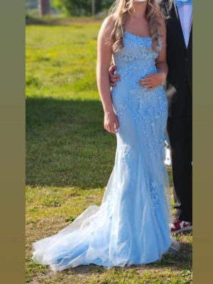 Ljusblå balklänning / studentklänning med släp ✨ - Elegant ljusblå långklänning med tunna axelband och öppen rygg. Klänningen har vackra spetsapplikationer och blommiga broderier över hela tyget samt en lätt utsvängd kjol med släp. Perfekt för bal eller student. Använd endast 1 gång. Pris går att diskutera🥰