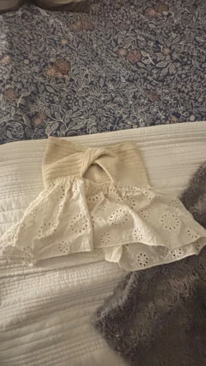 Vit broderad bandeau topp - Supersöt bandeau topp i vitt med broderade blommor och volang. Överdelen är stickad och ger en snygg kontrast till den luftiga, broderade nederdelen. Perfekt för sommarens alla tillfällen!