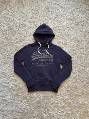 Superdry hoodie blå - Snygg hoodie från superdry med feta detaljer, använd men i gott skick. Storlek S, tveka inte på o skriva vid fler frågor!