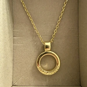Guldfärgat cirkelhalsband Snö of Sweden - Snyggt halsband i guldfärg från Snö of Sweden med en rund cirkelberlock. Berlocken har texten 'SNÖ OF SWEDEN' ingraverad längs kanten. Kedjan är tunn och elegant, perfekt för att ge en stilren touch till din outfit.