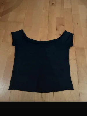 Marinblå offshoulder croppad topp från brandy Melville  - Trendig blå offshoulder topp med croppad passform. T-shirten har korta ärmar och en bred urringning som sitter snyggt över axlarna. Perfekt att styla med höga jeans eller kjol för en cool look.
