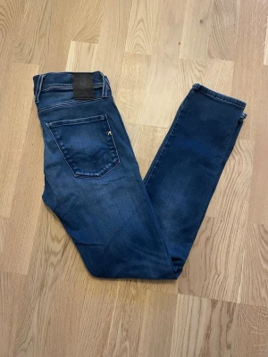 Mörkblå Replay Anbass W29 L32 - Jag säljer dom här Replay Anbass jeansen i storlek W29 L32. De är använda men fortfarande i fint skick. Tveka inte att höra av er!                     Mått: Längd=99cm. Midja=38cm