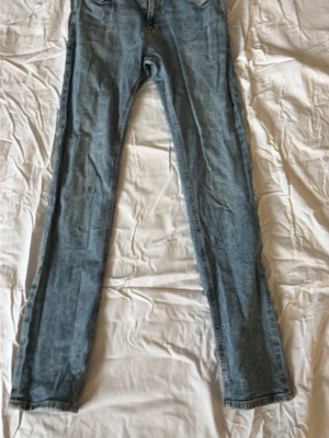 Ljusblå raka jeans - Säljer ett par ljusblå jeans med rak passform och klassisk femficksdesign. Jeansen har normal midja och är tillverkade i ett mjukt denimtyg som passar perfekt till en avslappnad stil.