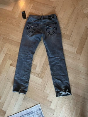 Grå True Religion jeans med slitna benslut - Säljer ett par grå jeans från True Religion använt under sommarn lite slit vid hälarna lapp kvar annars felfria vagga/relaxed bootcut