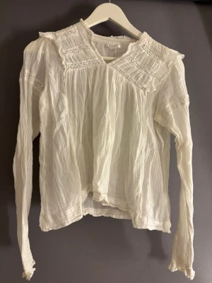 Vit romantisk blus från Gina Tricot - Söt vit blus från Gina Tricot med långärmad design och fina spetsdetaljer vid axlar och bröst. Tillverkad i ett tunt, krinklat tyg som ger en luftig känsla. Perfekt för dig som gillar en romantisk och bohemisk stil.