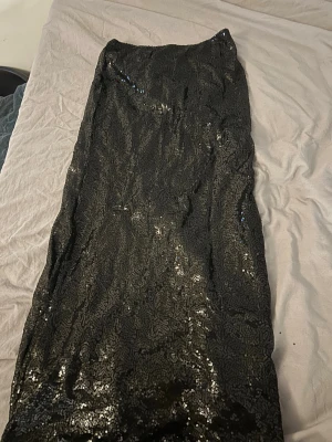 Svart glittrig långkjol med slits - Säljer en svart långkjol med glittriga paljetter med slits baktill. Använde en gång på nyår köpt ifrån Nelly nypris ca 200kr