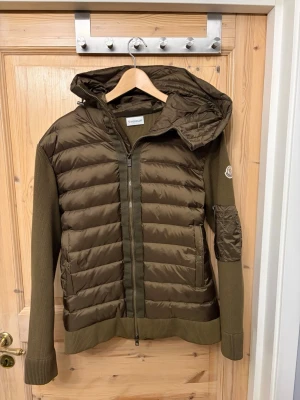 Olivgrön dunjacka från Moncler stl s - Snygg olivgrön dunjacka från Moncler med quiltad framsida, stickade ärmar och huva. Jackan håller även värmen på vinter ungefär till -6 , priset kan diskuteras, den e helt ny använd 1 gång