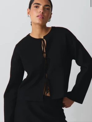 Svart knytkofta med lång ärm - Trendig svart kofta med lång ärm och tre knytningar framtill. Rak passform och rund halsringning. Perfekt att styla över ett linne eller topp för en cool look. Tröjan är använd fåtal gånger och i mycket fint skick. 