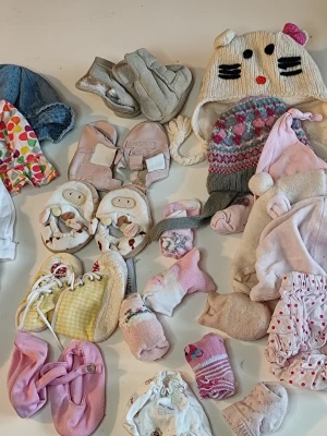 Sött mösspaket för baby - Paket med flera baby- och småbarnsmössor i olika färger och mönster, bland annat en vit stickad mössa med kattansikte och öron, en rosa/vit mönstrad mössa med tofs samt tunna bomullsmössor med prickar och knyt. Perfekt för att hålla huvudet varmt och stiligt.