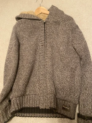 Varm gråbeuge cardigan från blueprint - Mysig gråmelerad stickad hoodie från Blueprint med dragkedja framtill och huva. Tröjan har ribbstickade muddar och en mjuk, lurvig insida i huvan. Perfekt för kalla dagar och vintern!!💕💕