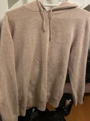 Beige cashmere hoodie från Sayless - Mysig beige hoodie från Sayless i mjuk cashmere. Klassisk modell med huva och dragsko, ribbade muddar vid ärmslut och nederkant. Perfekt för dig som vill ha en stilren och bekväm hoodie i ett lyxigt material. Den är 100% cashmere