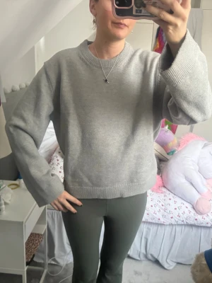 Ljusgrå stickad tröja - En basic ljusgrå stickad tröja med rund halsringning och ribbade muddar. Tröjan har en rak passform och är perfekt för lager-på-lager. Enkel och stilren design som funkar till det mesta.