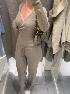 Beigeset ribbat loungewear-set - Mysigt ribbat loungewear-set i beige med omlottopp och långa ärmar samt matchande byxor med dragsko i midjan. Perfekt för chill dagar hemma eller när du vill vara bekväm men ändå snygg. Mjuk stretchig kvalitet som sitter skönt på kroppen.