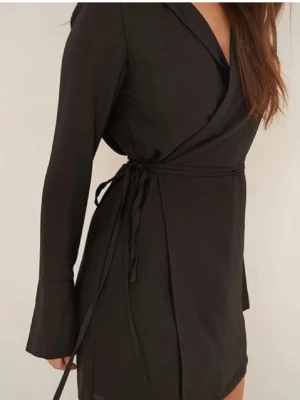 Svart omlottklänning med snörning - Snygg svart omlottklänning med knytband i midjan som ger en cool och figurnära passform. 