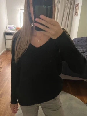 Stickad tröja 2 i 1  - En svart stickad tröja med v-ringad hals och lång ärm. Men man kan även vända på den så man får en tröja med öppen rygg. Modellen är loose fit och har en enkel, stilren design utan synliga detaljer. Perfekt att slänga på sig när det är lite kyligt ute. Passar dig som gillar basic och bekvämt.