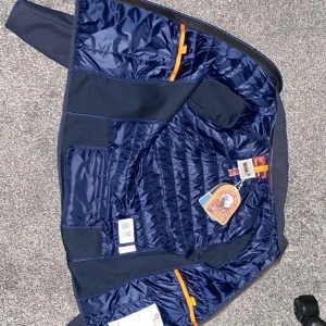 Mörkblå Parajumpers pufferjacka Y-M - Snygg mörkblå pufferjacka från Parajumpers med quiltad insida och coola orange detaljer. Jackan har dragkedja och klassisk PJS-logga på insidan. Perfekt för dig som vill ha en stilren och sportig look under höst och vinter.