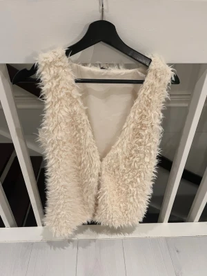 Beige fluffig pälsväst - Säljer en beige fluffig pälsväst med mjuk och lurvig yta. Västen har en enkel, ärmlös design. Perfekt för dig som vill ha en mysig och trendig look med lite extra edge.