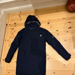 Helt Ny! Mörkblå parkas från Didriksons - Säljer en oanvänd mörkblå parkas från Didriksons med huva, stora fickor framtill och dragkedja. Jackan är 100% vattentät och har reflekterande detaljer på ärmarna. Perfekt för kalla dagar och har en clean, stilren look. Priset kan diskuteras vid snabb affär.