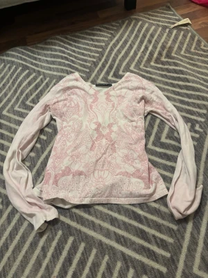 Ljusrosa blommig långärmad topp - Säljer en ljusrosa långärmad topp med v-ringning och blommigt mönster i rosa på framsidan. Toppen är i mjuk bomull och har en feminin, normal passform. 