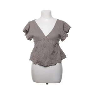 Beige/ grön blus med v-ringning och knyt - Säljer en söt beige/grön blus med v-ringad hals och korta volangärmar. Toppen är ifrån lager 157 och har ett bra skick, den är i strl xs! Skriv för egna bilder!