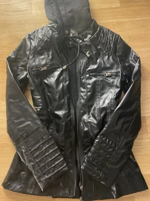 Yk2 style skinnjacka - Cool skinnjacka i svart och brun med hoodie och snörning i halsen. Jackan har dragkedja framtill, två fickor med dragkedja på bröstet och snygga detaljer på ärmarna. Passformen är normal och jackan har långa ärmar. Perfekt för dig som gillar streetstyle. Båda för 1200kr och en för 800kr, pris kan diskuteras vid snabb försäljning.