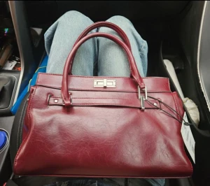 Vinröd handväska från Bershka - Snygg vinröd handväska från Bershka i skinnimitation med stilrena silverdetaljer och dubbla handtag. Väskan har en klassisk, boxig form och ett rymligt innerfack med dragkedja. Perfekt för dig som gillar att ha med dig allt du behöver och vill ha en chic look.