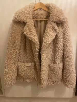 Beige teddyjacka  - Säljer en fluffig beige teddyjacka med bred krage och två stora fickor framtill. Jackan har mjukt pälsliknande material. Är storlek xs men funkar super på mig som vanligtvis har s! Har använts någon enstaka gång