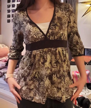Blommig topp med v-ringning - Säljer en blommig topp i beige, brun och gröna toner med v-ringad hals och bred midjedetalj. Blusen har trekvartsärm och ett flowigt fall. Materialet känns som mjuk bomull eller polyester. Perfekt för dig som gillar mönstrade toppar med lite extra detaljer.