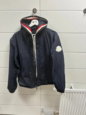 Moncler marinblå vindjacka med huva - Säljer en moncler vindjacka. Jackan har två små hål. Den är äkta! 