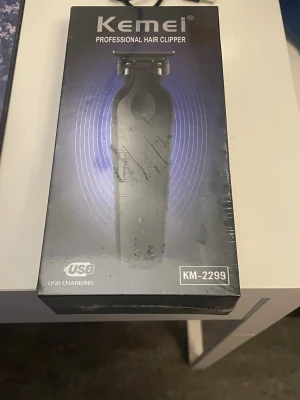 Kemei professionell hårtrimmer KM-2299 - Kemei KM-2299 är en svart elektrisk hårtrimmer med stålblad, statuslampa och USB-laddning. Den har transparent fuselage, tre svarta kammar, rengöringsborste och laddningskabel. Passar både hår, skägg och kropp. Batterikapacitet 1200mAh och laddningstid 180 min.