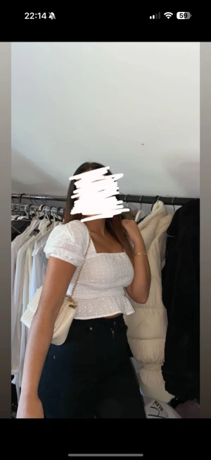 Vit blus med volang från NA-KD - Superfin vit blus från NA-KD med puffiga korta ärmar och volang nedtill. Blusen har broderade små blommor i tyget och smock över midjan för en snygg passform. Perfekt för dig som gillar romantisk och feminin stil.