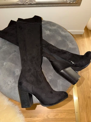 Svarta höga stövlar med klack - Säljer ett par svarta, höga stövlar med grov klack och rund tå. De är tillverkade i mjuk mocka och har dragkedja på insidan för enkel påtagning. Snyggt stilrena och passar perfekt till höst- och vinterlooken. 9 cm