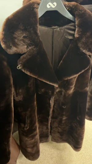 Mörkbrun pälsjacka med bred krage - Säljer en riktigt snygg mörkbrun pälsjacka med bred krage och klassisk knäppning. Jackan har en lyxig känsla och är perfekt för kalla dagar. Fodrad insida och diskreta fickor på sidorna. Passar dig som vill sticka ut med en statement-jacka.