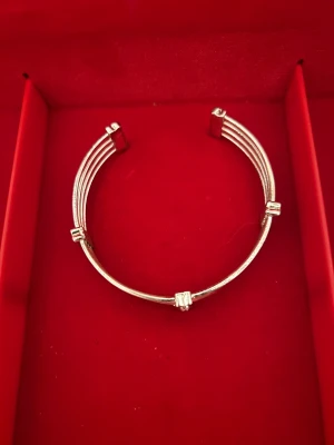 Silvrigt armband med glittriga stenar - Snyggt armband i silverfärgad metall med fyra parallella band och dekorativa rektangulära detaljer med infällda glittriga stenar. Stilren och modern design som ger en lyxig känsla. Perfekt för dig som gillar bling och vill sticka ut.