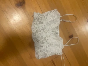 Vit spetsig linnetopp från FB Sister - Säljer en vit linnetopp från FB Sister i storlek S. Toppen har tunna axelband och är helt täckt av vacker spets med blommigt mönster. Perfekt för dig som gillar romantisk och feminin stil. Supersnygg att matcha med jeans eller kjol!
