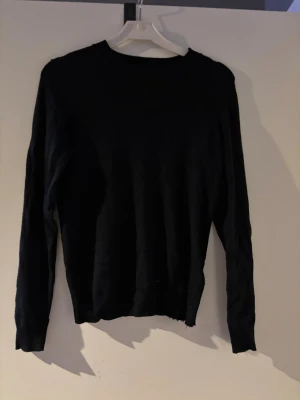 Svart stickad tröja från 157 XS - Svart stickad tröja från 157 i storlek XS. Tröjan har rund halsringning med ribbad kant och långa ärmar. Enkel och stilren design som funkar till många olika looks. Perfekt för dig som gillar basic och svart.