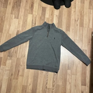 Grå half zip-tröja från Polo Ralph Lauren - Säljer en stilren grå långärmad tröja från Polo Ralph Lauren med half zip och klassisk broderad logga på bröstet. Tröjan har hög krage och är gjord i mjuk bomull. I princip nyskick med en enda liten defekt som visas på sista bilden och med tanke på den har jag valt att dra ner priset rejält, alltså väldigt prisvärd. Även bara använd ca 3 gånger för att den inte passade.