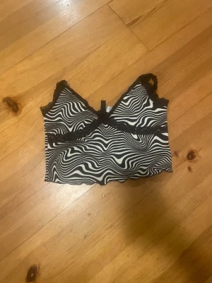 Zebramönstrad croppad topp H&M Divided - Säljer en croppad zebramönstrad topp från H&M Divided i svart och vitt. Toppen har spetsdetaljer vid axelbanden och runt bröstet, samt en v-ringad form. Perfekt för dig som gillar att sticka ut med coola mönster och snygga detaljer.