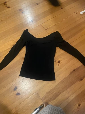 Svart offshoulder topp med lång ärm - Säljer en svart offshoulder topp med långa ärmar. S/M Toppen har en snygg, bred halsringning som visar axlarna och är figurnära i modellen. Perfekt för dig som gillar stilrena och enkla plagg med lite edge.