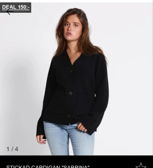 Svart stickad kofta med knappar - Svart stickad kofta från Sabrina med v-ringad hals och stora knappar framtill. Koftan har två fickor och långa ärmar med ribbade muddar. Perfekt för lager-på-lager och chill stil. Snygg till jeans eller kjol.