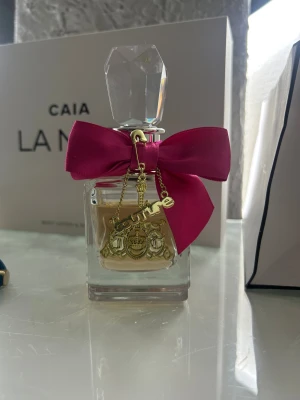 Juicy Couture parfym med rosett - Snygg parfymflaska från Juicy Couture med en rosa rosett och guldfärgade detaljer. Perfekt för dig som gillar trendiga accessoarer och vill ha något som sticker ut på hyllan. Ny pris 900