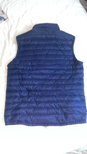 väst  - Säljer en snygg och varm marinblå dunväst i storlek M. Västen är i mycket fint skick, knappt använd och utan några skador eller fläckar. Perfekt för vår, höst och kyliga sommarkvällar.